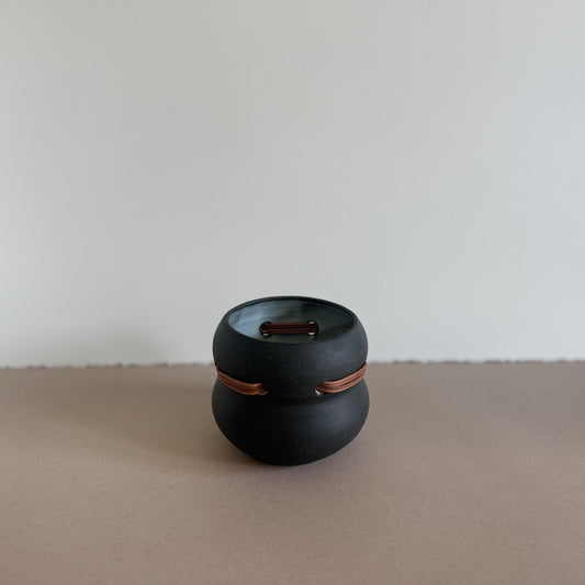 Black ceramic container woven with tan leather cord on a beige surface